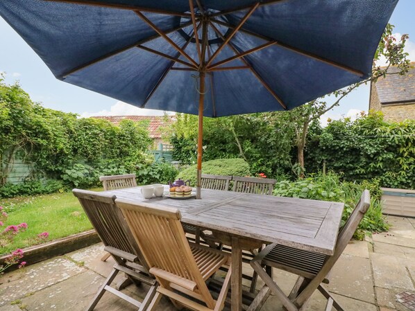 A wooden table with chairs and a large blue umbrella in a garden setting. - Pippins Loders (Bridport)