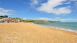 A beach with a clear sky, a sandy shore, and a few buildings in the background. - Outlook Lodge (Weymouth)