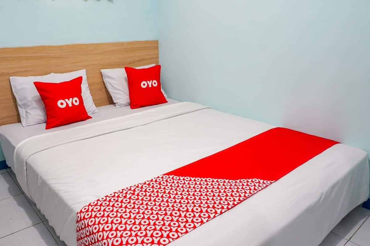 Une chambre d’hôtel avec une tête de lit en bois, du linge de lit blanc et des touches de couleur rouge, notamment sur les coussins et la couverture.