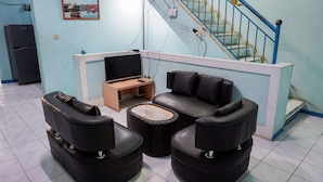 A room with a sofa, two armchairs, a coffee table, a TV, and a staircase with blue railings. - OYO 2088 Grha Blue Sky Syariah (Bandung)