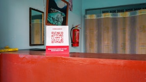 A red reception desk with a QR code and text on a white sign. - OYO 2088 Grha Blue Sky Syariah (Bandung)