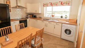 A compact kitchen with a dining area, a built-in oven, a washing machine, and a window with a view. - Llain Bach (Llangefni)