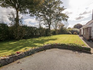Set amidst lush greenery, this serene property features a stone building with a pitched roof, surrounded by mature trees and shrubs.