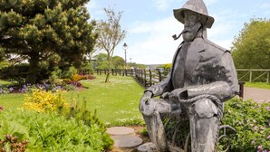 A statue of a seated figure in a park with a bench, surrounded by greenery and flowers. - Chapel Cottage (Filey)