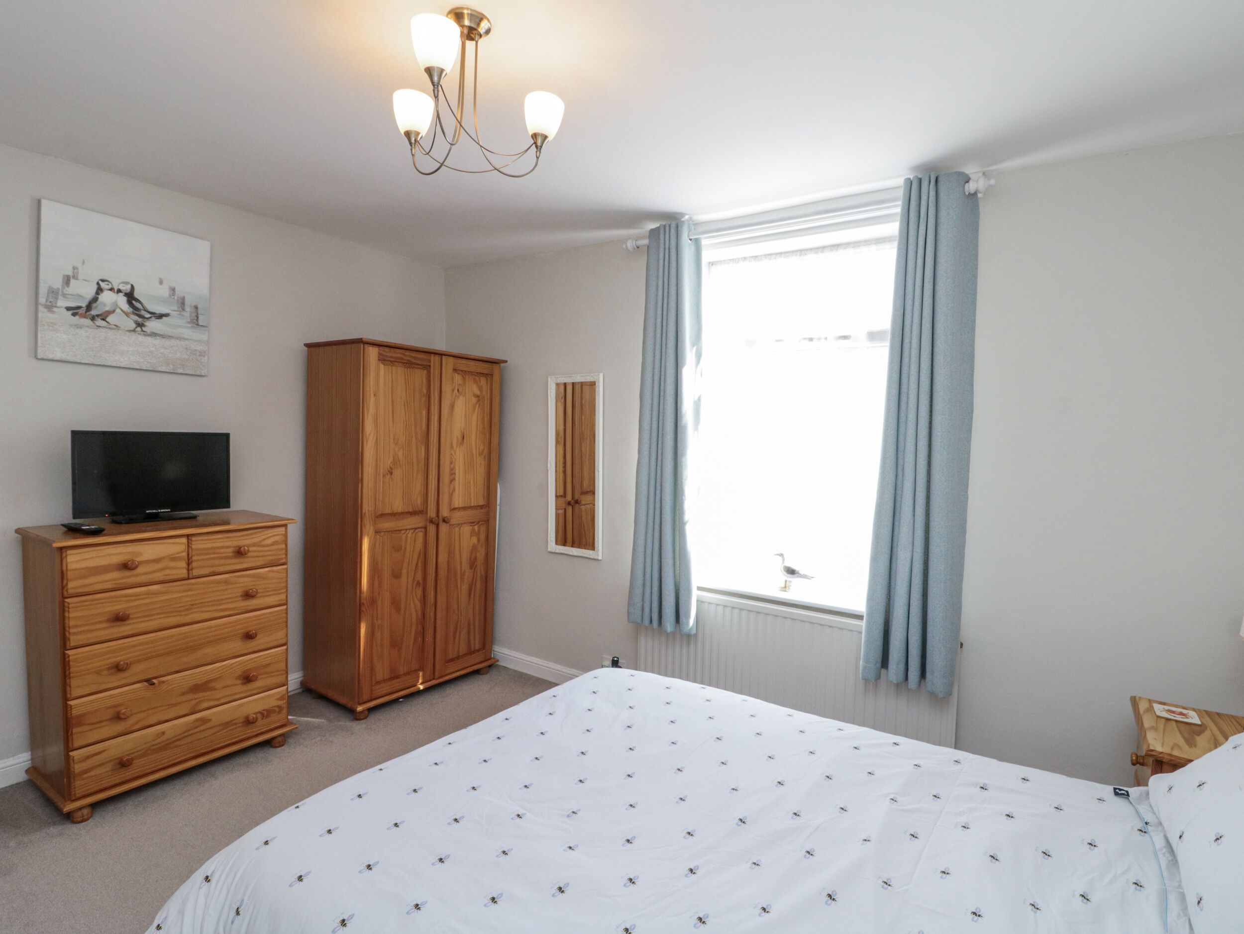 A bedroom with a bed, dresser, TV, wardrobe, window, and curtains.