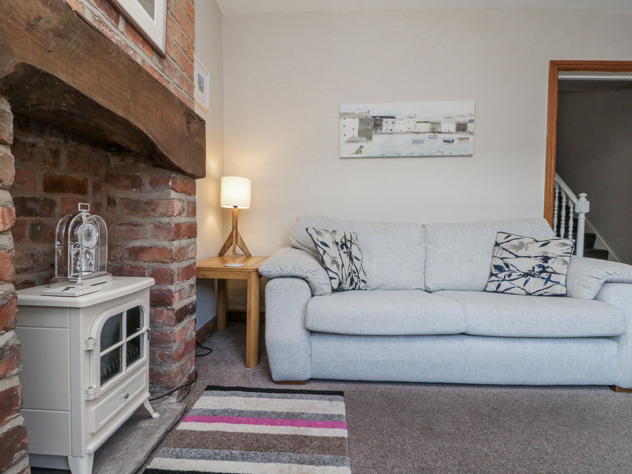 A cozy living room with a white sofa, a wooden side table, a lamp, and a decorative clock.