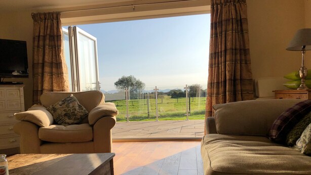 A living room with a sofa, a chair, a wooden table, and a television. - Rhos Y Foel Cottage (Pwllheli)