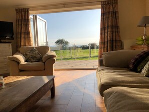 A living room with a sofa, a chair, a wooden table, and a television. - Rhos Y Foel Cottage (Pwllheli)
