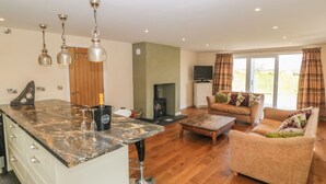 A spacious living area with a large island, a fireplace, and a comfortable sofa. - Rhos Y Foel Cottage (Pwllheli)