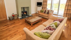 A cozy living room with a fireplace, a sofa, a television, and a large window. - Rhos Y Foel Cottage (Pwllheli)