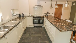 A kitchen with a central island, stainless steel appliances, and pendant lighting. - Rhos Y Foel Cottage (Pwllheli)