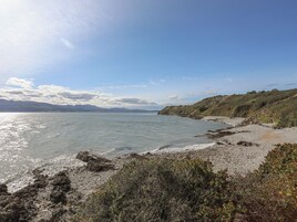 A coastal landscape with a rocky beach, clear sky, and distant mountains.