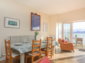 A dining area with a table set for four, wooden chairs, a vase with flowers, and a large framed sign on the wall. - The Old Lifeboat House (Beaumaris)