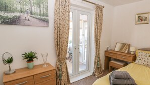 A bedroom with a wooden dresser, a bed with a yellow bedspread, a bedside table with a lamp, a mirror, and a framed picture on the wall. - Bumble Bee Cottage (Skegness)