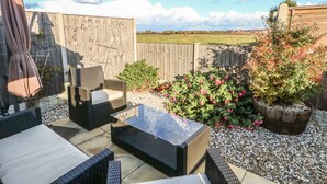 A patio with wicker furniture, a glass table, and a potted plant. - Bumble Bee Cottage (Skegness)