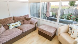 A sunroom with a large window, a striped sofa, a bench, and a chair. - Bumble Bee Cottage (Skegness)