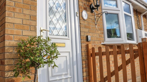 A brick house with a white door, a small window, and a wooden fence. - Bumble Bee Cottage (Skegness)