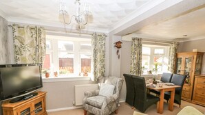A living room with a television, a fireplace, a dining table with chairs, and a cabinet. - Bumble Bee Cottage (Skegness)
