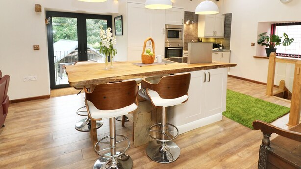 A modern kitchen with a wooden island, bar stools, and pendant lighting. - The Cart House (Liskeard)