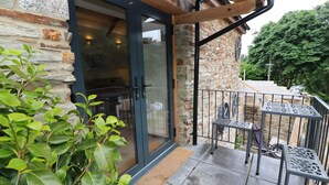 A stone building with a glass door and a small outdoor patio with metal chairs and a table. - The Cart House (Liskeard)