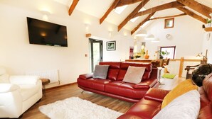 A living room with a red leather sofa, a white sofa, and a white rug. There is a flat-screen TV mounted on the wall. - The Cart House (Liskeard)