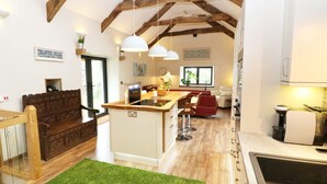 A spacious kitchen with wooden beams, a central island, and a dining area with red chairs. - The Cart House (Liskeard)