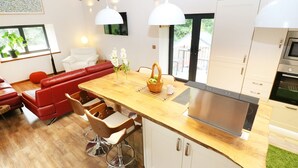 A modern kitchen with a wooden island, stainless steel appliances, and a red leather sofa in the living area. - The Cart House (Liskeard)
