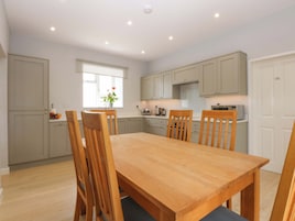 A modern kitchen with grey cabinets, a wooden dining table, and chairs. There is a window with a plant on the windowsill.