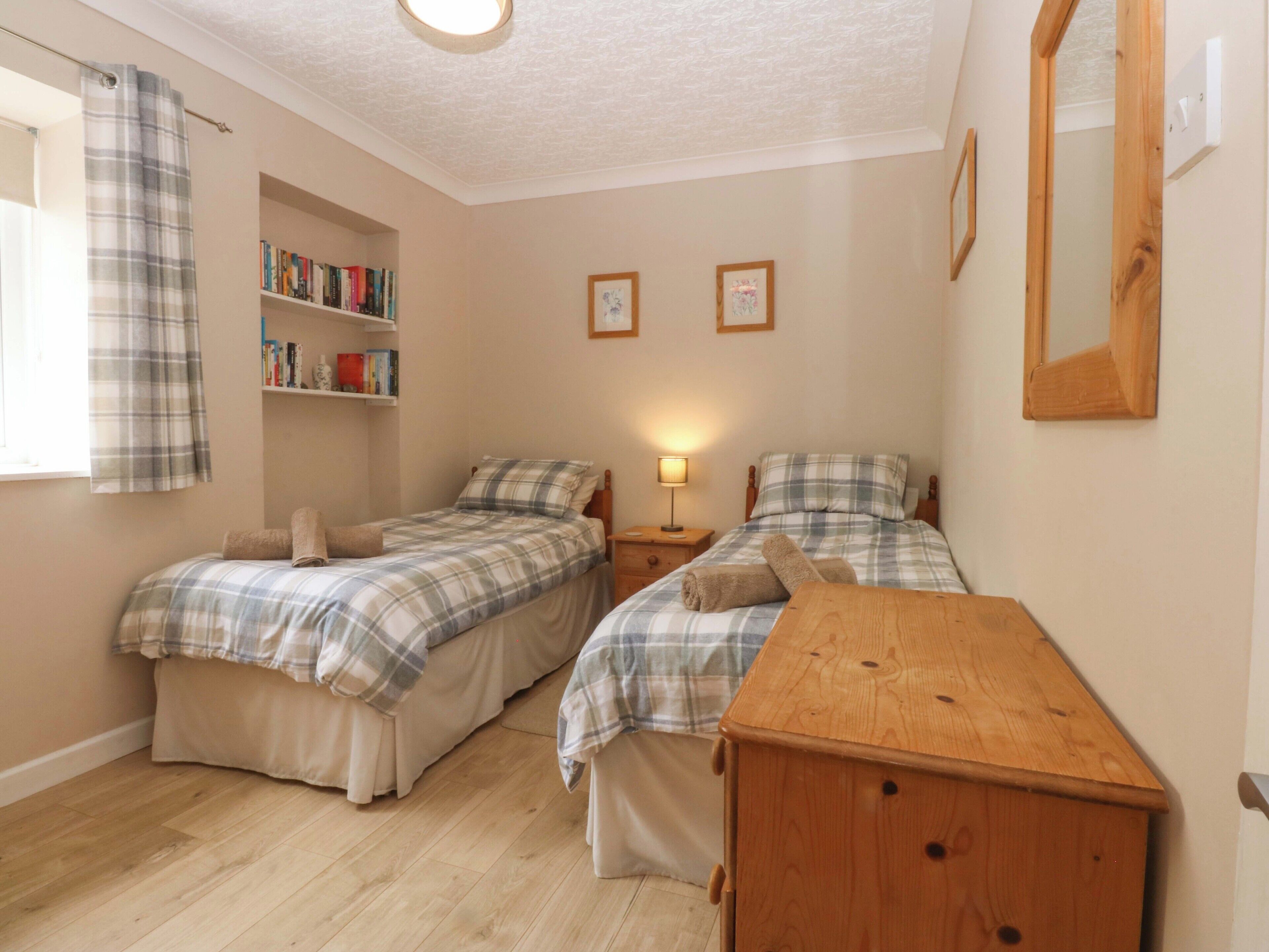 A bedroom with two beds, a wooden dresser, a bookshelf, and a window with a curtain.