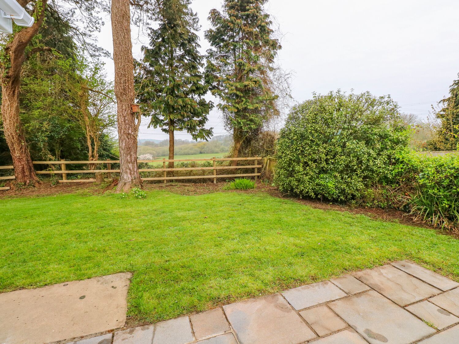 A well-maintained grassy area with a wooden fence, stone pathway, and various trees and shrubs.
