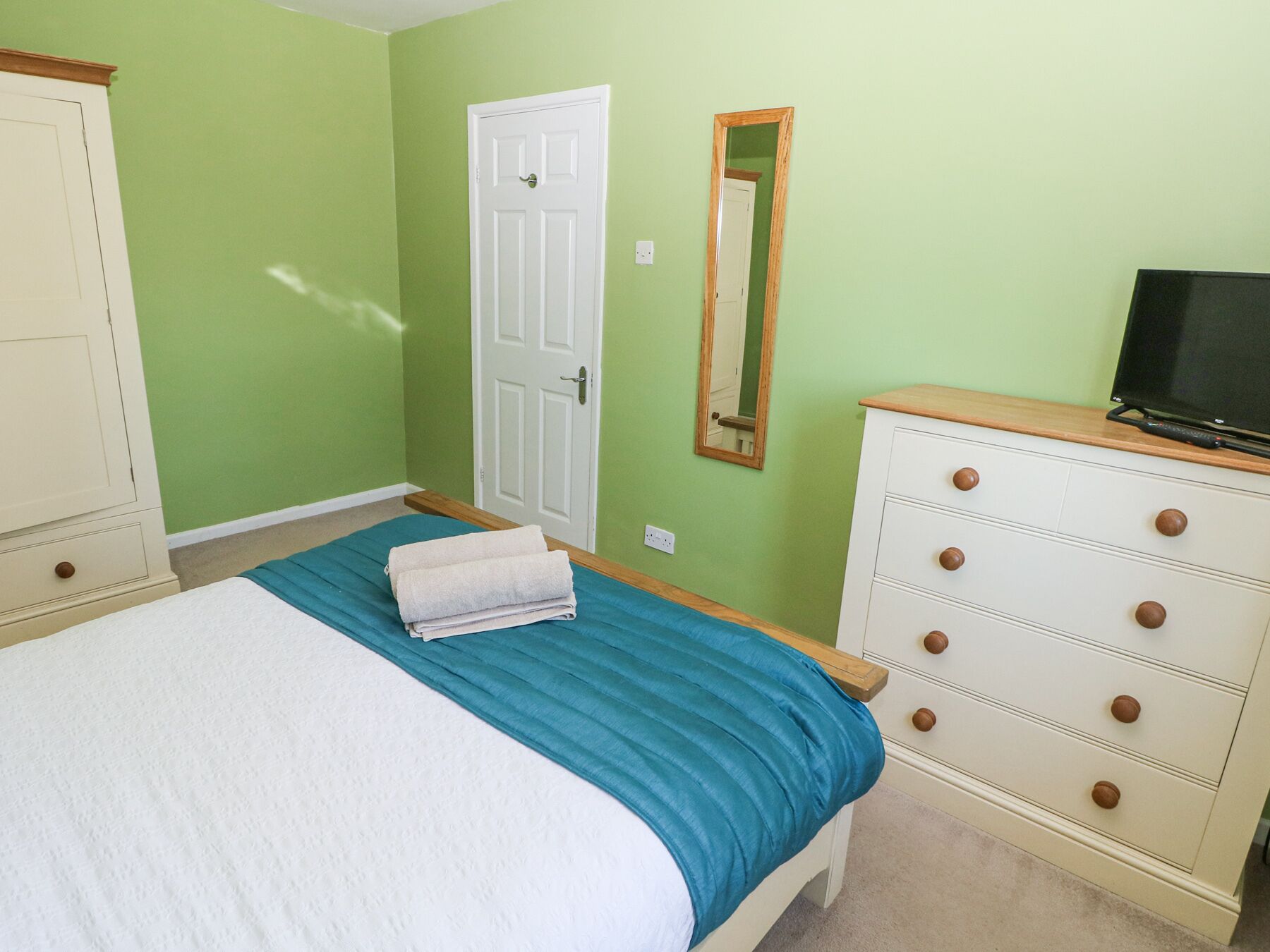 Une chambre à coucher avec un lit, une commode, un téléviseur et une porte.