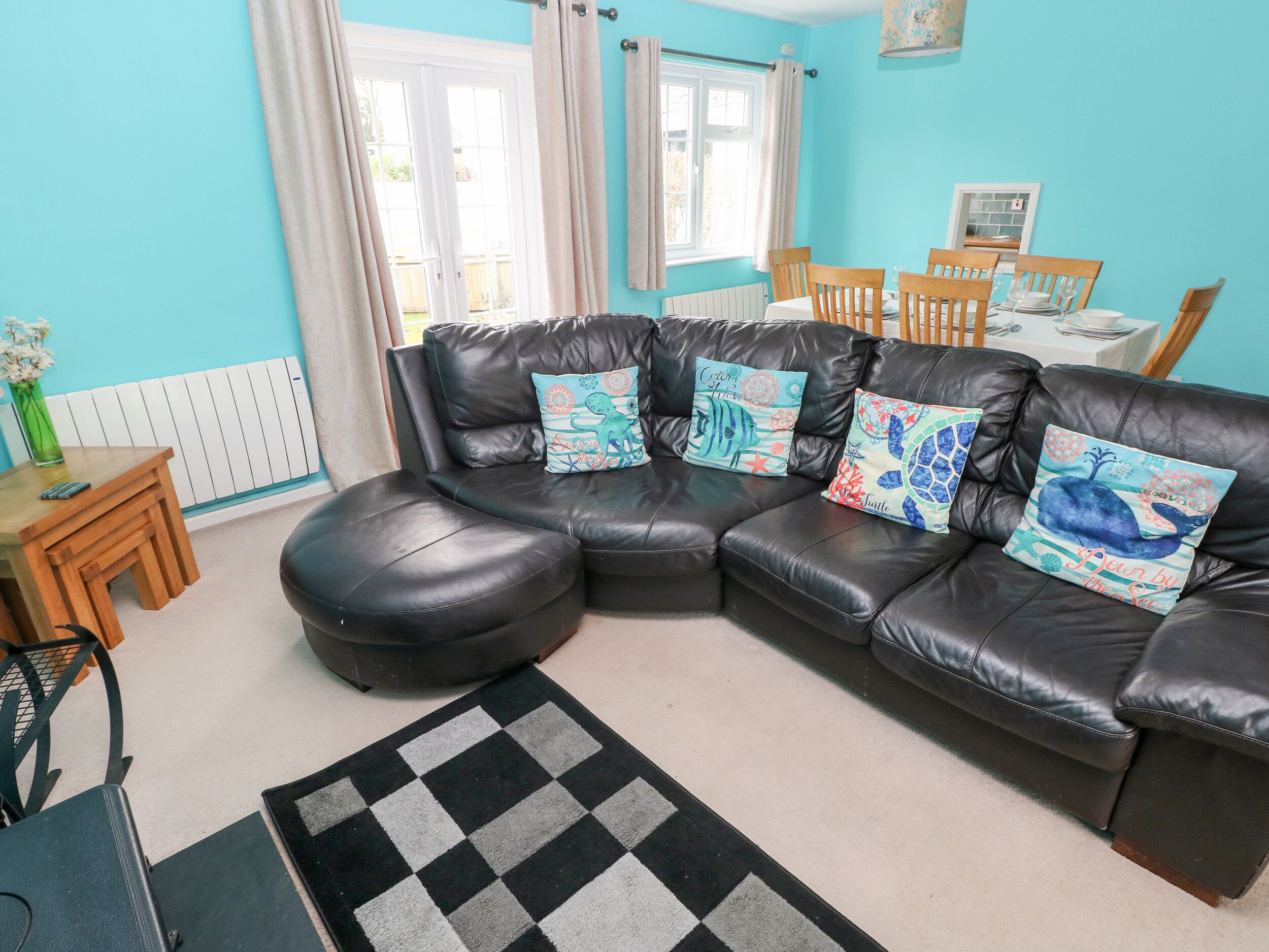 A modern living room with a black leather sectional sofa, a checkered rug, and decorative pillows.