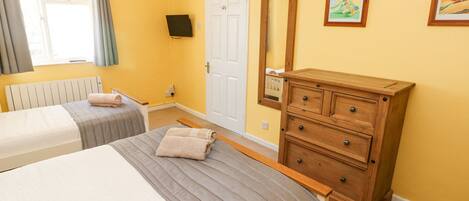 A bedroom with two beds, a wooden dresser, a white door, and two framed pictures on the wall.