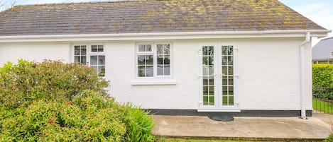 A single-story white building with a tiled roof, a front door, and a small porch area.