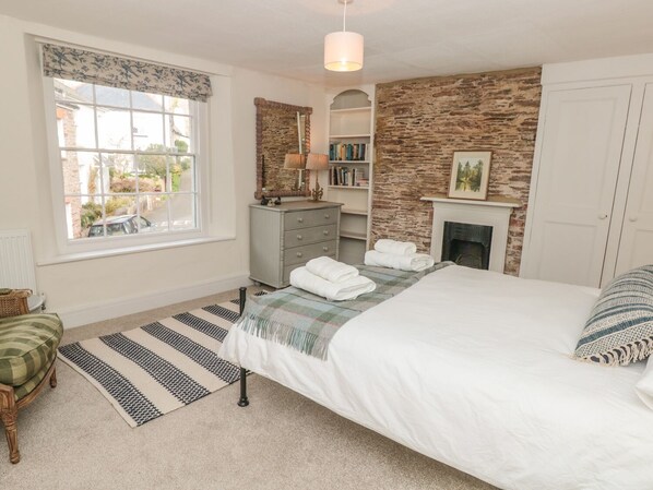A bedroom with a bed, a dresser, a fireplace, and a window with a view of the outside.