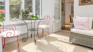 A bright room with a glass table, red chairs, a wicker sofa, and a door leading to another room. - Rosevine (Kingsbridge)