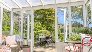 A conservatory with a glass roof, wicker furniture, and a view of a garden. - Rosevine (Kingsbridge)