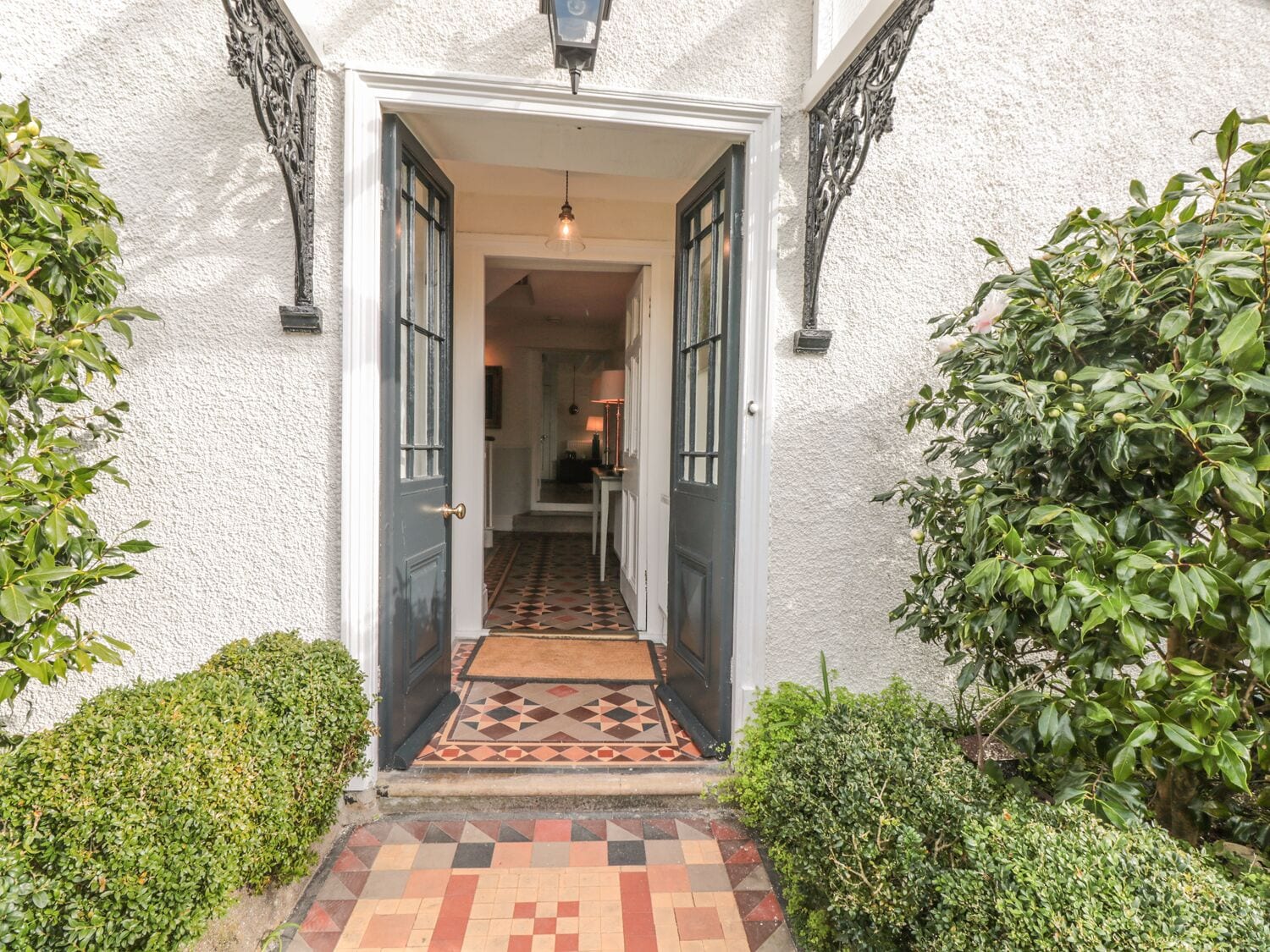A building entrance with a door, a patterned mat, and a light fixture above.