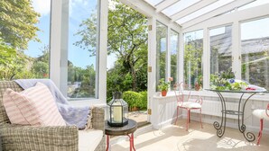 A conservatory with wicker furniture, a glass table, and potted plants. - Rosevine (Kingsbridge)