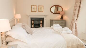 A bedroom with a bed, a bedside lamp, a dresser, a mirror, and a fireplace.