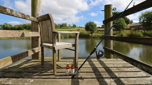 A wooden chair and a fishing rod on a dock with a calm river in the background.