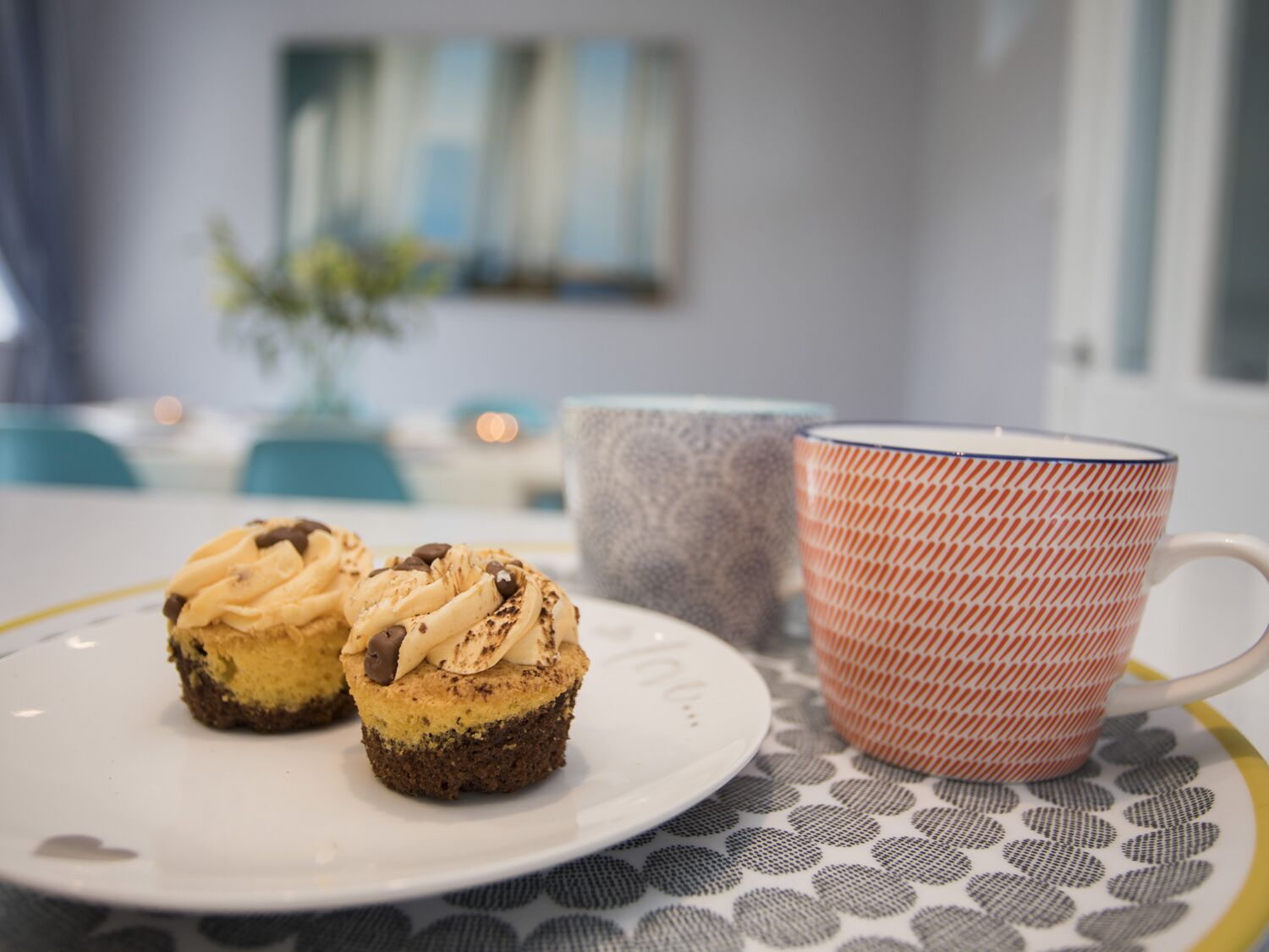 Une assiette avec deux petits gâteaux et une tasse à motifs, posée sur une table avec un dessous de verre décoratif.