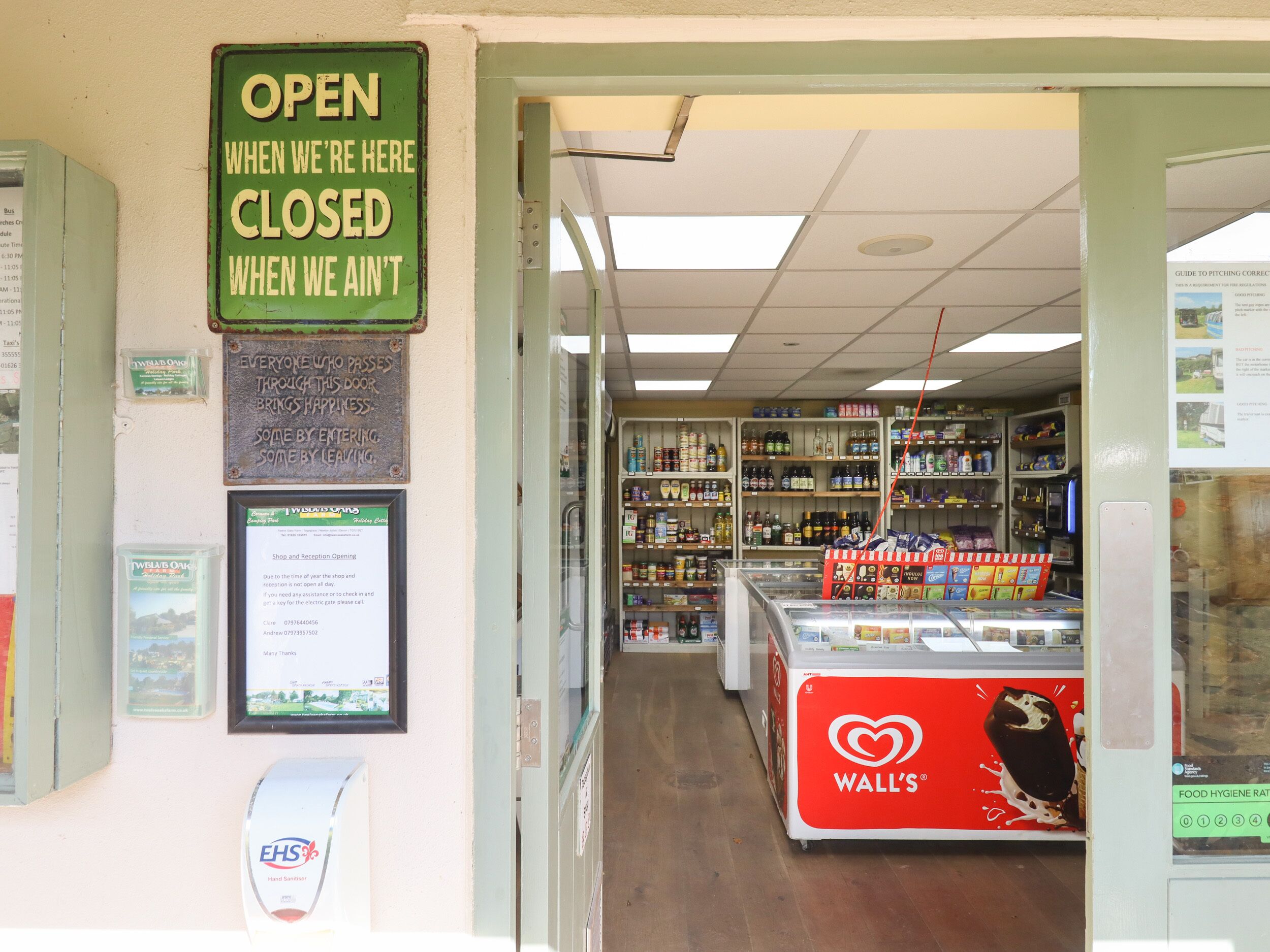 A store interior with shelves stocked with various products, a sign indicating the store is open when closed, and a hand sanitizer dispenser.