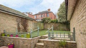 A brick patio with a small staircase leading to a garden area, surrounded by a wooden fence and a brick wall. - Casa Carmen (Weymouth)