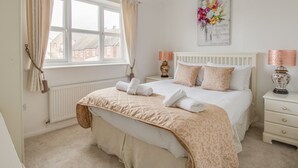 A bedroom with a large bed, a window with curtains, a bedside table with a lamp, and a wall decoration. - Casa Carmen (Weymouth)