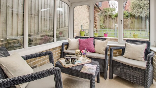 A sunroom with wicker furniture, a glass coffee table, and a view of a garden. - Casa Carmen (Weymouth)