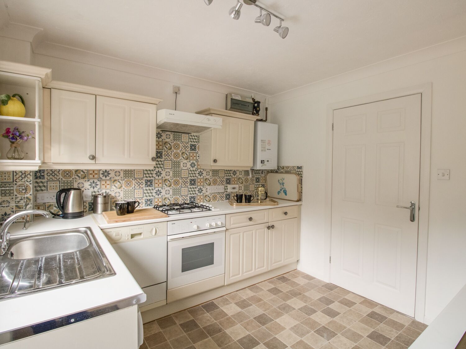 A small kitchen with white cabinets, a gas stove, a sink, and a patterned backsplash.
