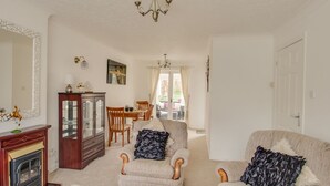 A cozy living room with a fireplace, two armchairs, a coffee table, and a dining area with a table and chairs. - Casa Carmen (Weymouth)