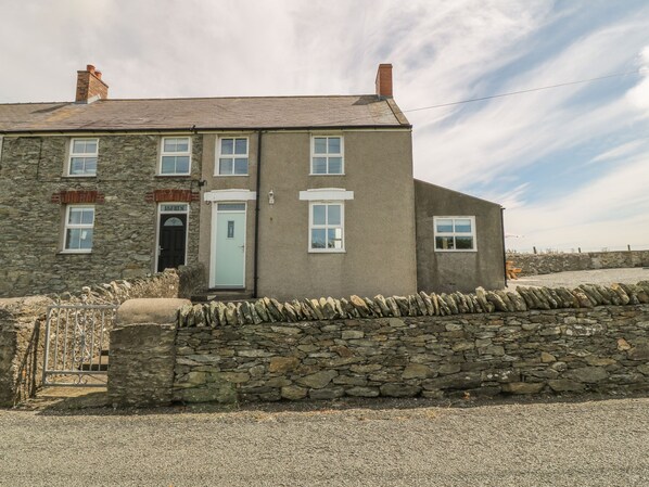 A two-story stone building with a stone wall in front, a metal gate, and a clear sky. - Glasfryn (Holyhead)
