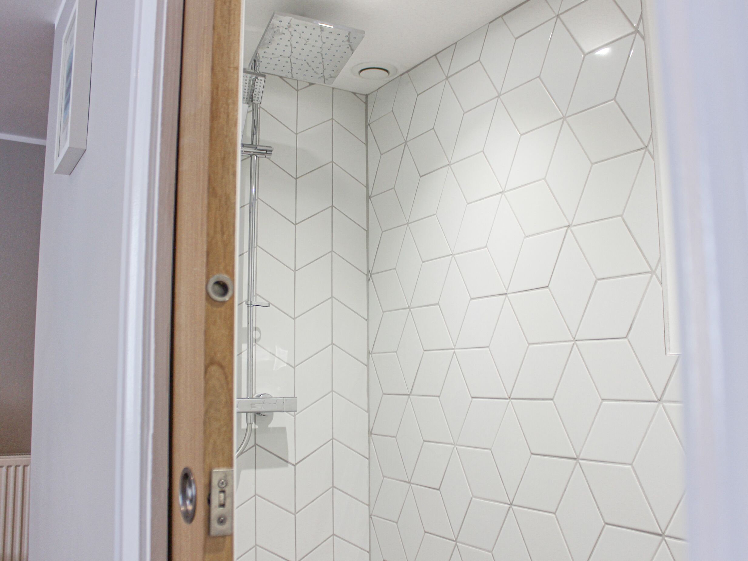 A shower with a geometric tile pattern and a wooden door frame.
